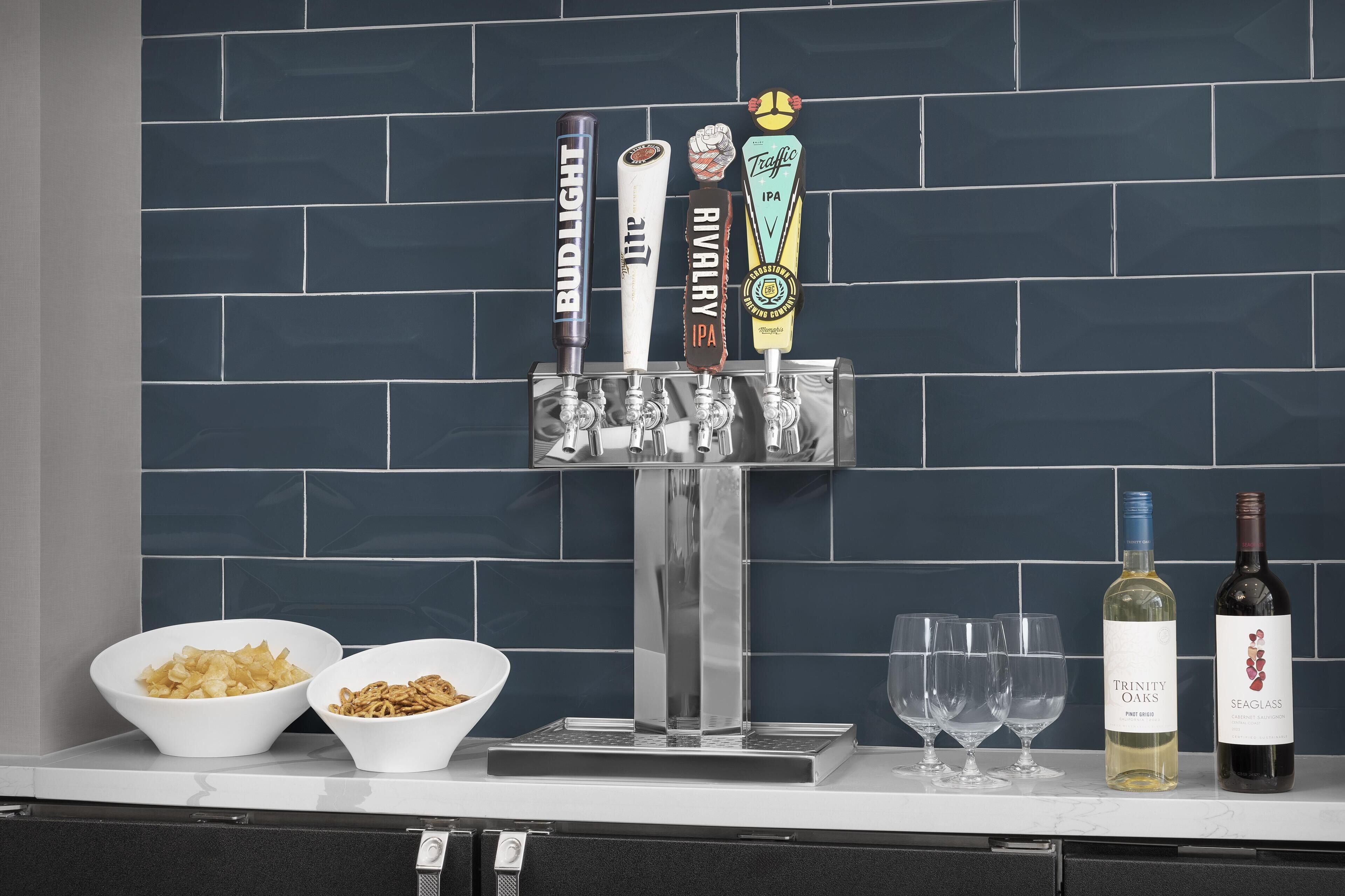 A bar area with beer taps, glasses, bowls of snacks, and bottles of wine.