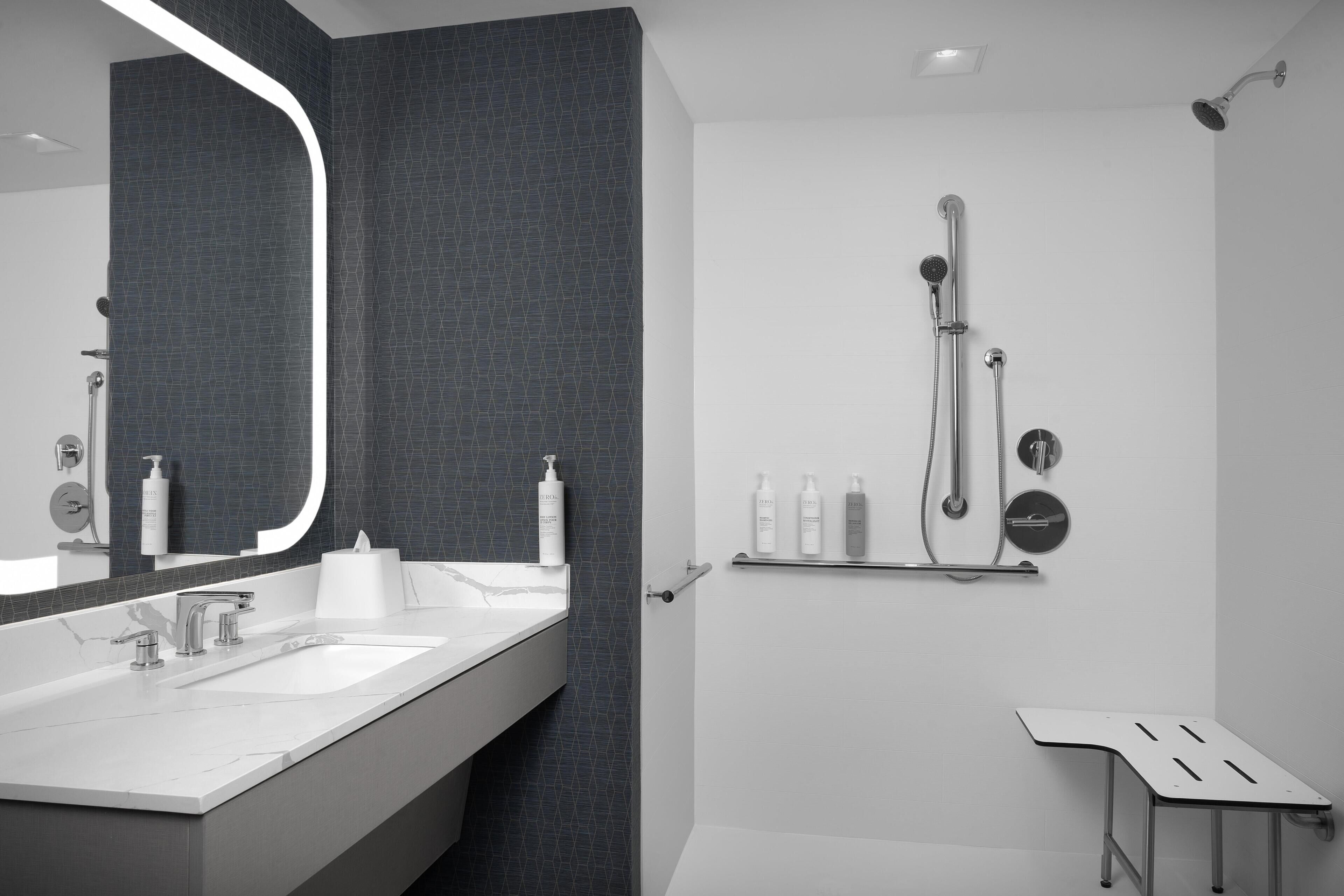 A modern bathroom with a large mirror, dual sinks, a shower with a handheld showerhead, and a towel rack.