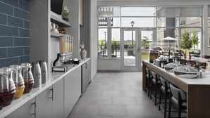 A modern kitchen with a long counter, stainless steel appliances, and a view of the outdoors through large windows. - Homewood Suites by Hilton Jackson (Jackson)
