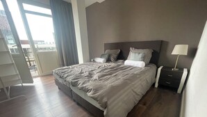 A modern bedroom with a large bed, a nightstand, a lamp, and a view of the outdoors. - Topsleep Apartments 26-1 (Arnhem)