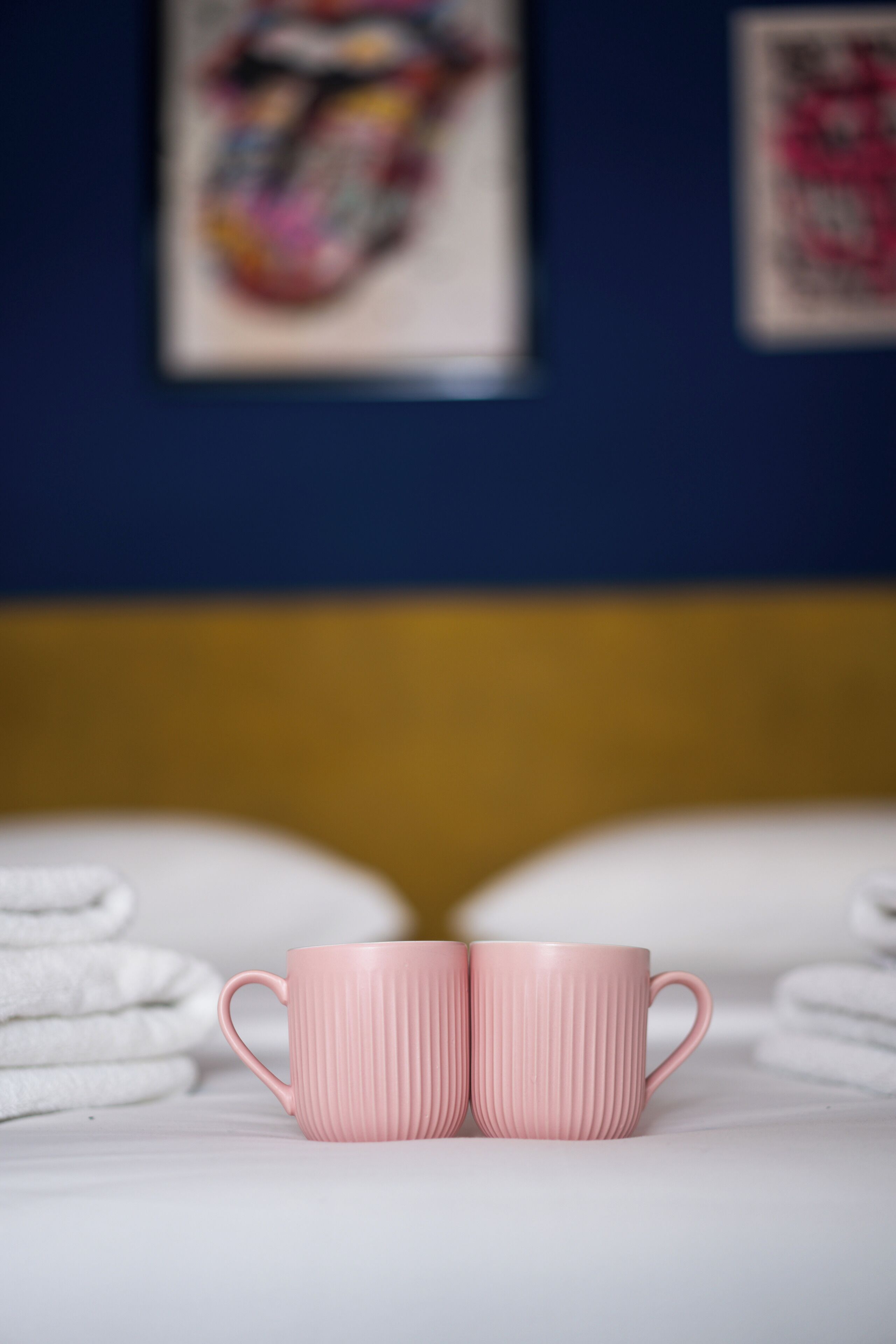 Duas chávenas rosa com textura em canaletas sobre uma superfície branca, com toalhas ao fundo.