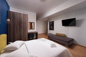 A modern hotel room with a bed, a desk, a sofa, and a TV.