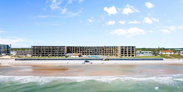A multi-story hotel with balconies, a pool, and a beach view. - Cozy Condo with Direct access to our Beautiful Beach, Tiki Bar and Heated Pools! (Daytona Beach Shores)