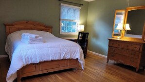 Une chambre à coucher avec un lit en bois, une table de chevet, une commode et une fenêtre avec des stores.