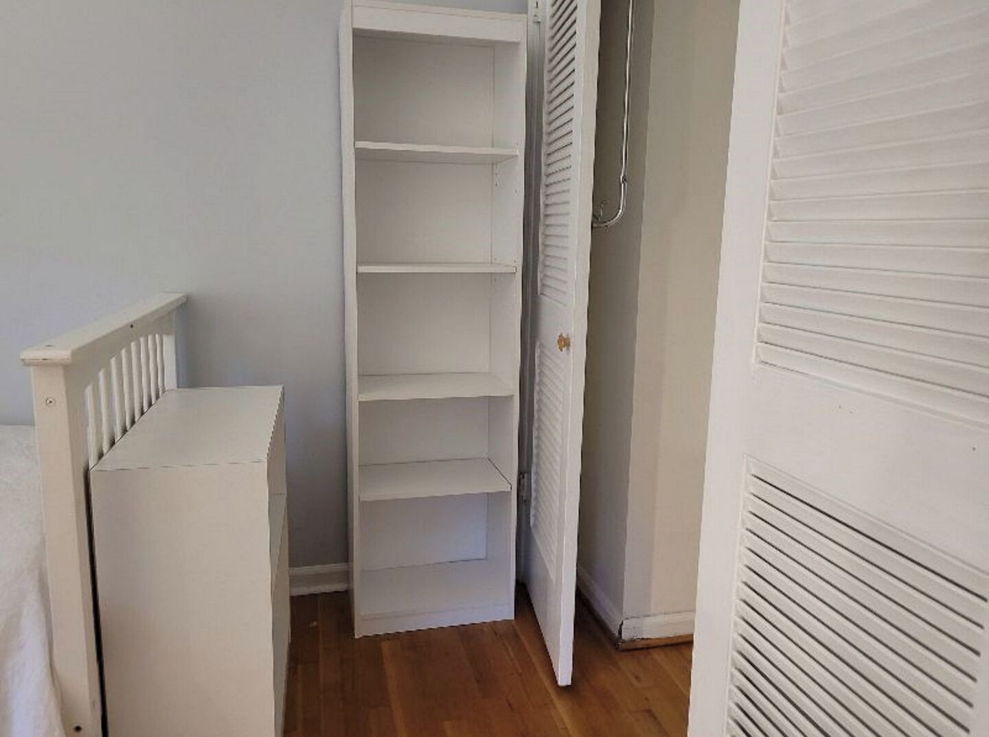 Une pièce avec une armoire blanche, une petite table blanche et un plancher en bois.