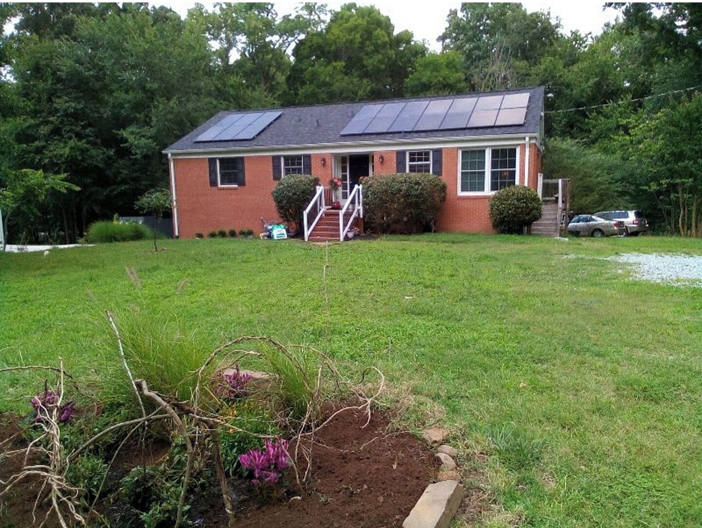 A single-story house with a brick exterior, a front porch, and solar panels on the roof.