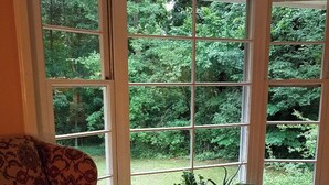 Une pièce dotée d’une grande fenêtre, d’un fauteuil à motifs et de plusieurs plantes en pot disposées sur le rebord de la fenêtre.