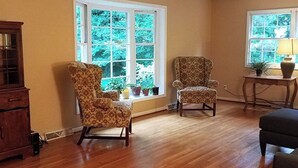 Une pièce dotée d’un plancher en bois, de deux fauteuils à motifs, d’une armoire et d’une table sur laquelle se trouvent une lampe et des plantes en pot.