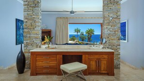 Une salle de bain avec un mur d’accent en pierre, un grand meuble-lavabo avec un miroir et une vue sur l’océan.