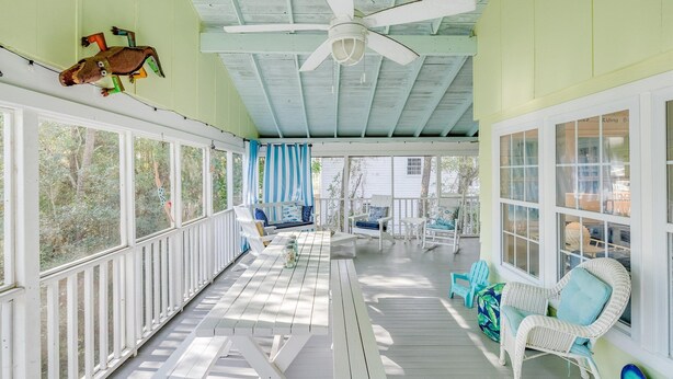 Eine überdachte Veranda mit weißen Geländern, einem Deckenventilator und Gartenmöbeln.
