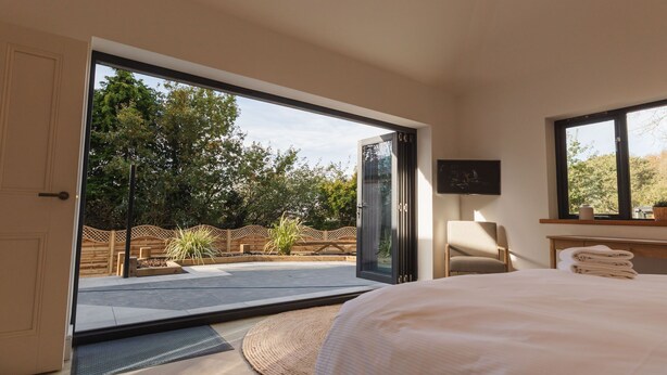 Un dormitorio con un amplio ventanal corredera que da a un patio, una cama, una silla y una mesita con toallas.