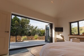 Una camera da letto con un'ampia porta scorrevole in vetro che si apre su un patio, un letto, una sedia e un tavolino con degli asciugamani.