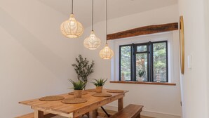 Una mesa de comedor de madera con individuales tejidos, tres lámparas colgantes tejidas y un ventanal con vistas a follaje.