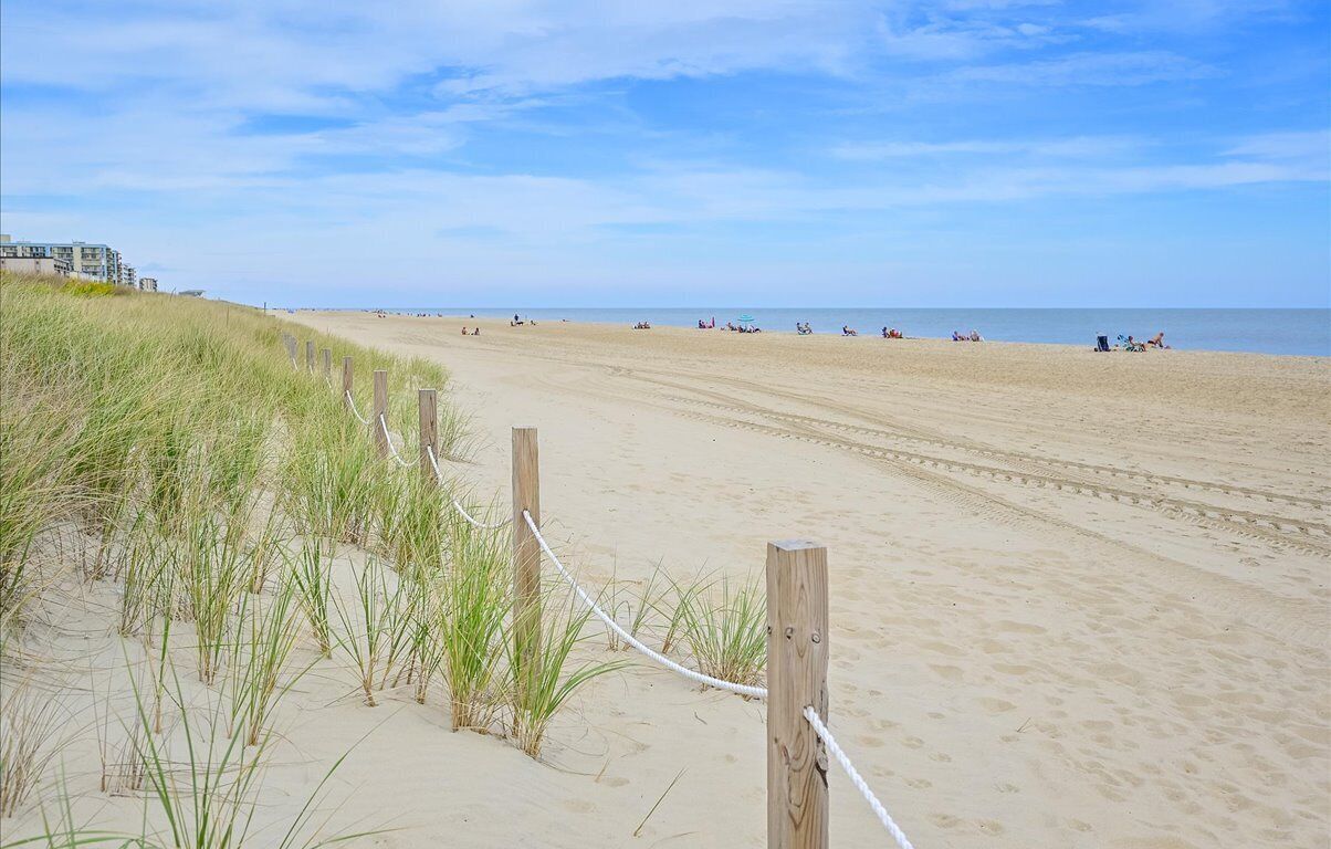 A wide sandy beach with a wooden fence and grass in the foreground.