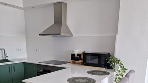 Eine moderne Küche mit einer zentralen Kochinsel, grünen Schränken, einer Edelstahl-Dunstabzugshaube, einer Mikrowelle und einem Blumentopf.