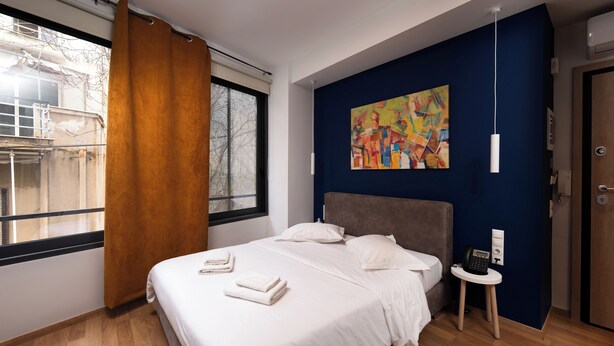 A modern hotel room with a large bed, a bedside table with a phone, and a window with curtains. - Athens luxury suite 26 m2  (Athina)