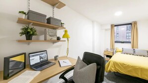 A hotel room with a desk, two laptops, a chair, a bed with a yellow bedspread, a window with curtains, and shelves with decorative items. - For Students Only Central Pl Sheffield (Sheffield)