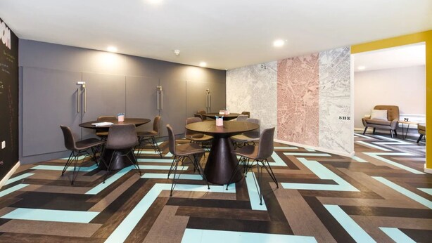 A modern conference room with round tables and chairs, a patterned floor, and a cityscape wall. - For Students Only Central Pl Sheffield (Sheffield)