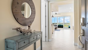 A hallway with a wooden console table, a large mirror, and a view of a balcony with outdoor furniture.