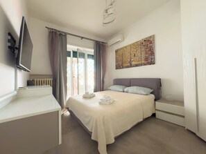 A bedroom with a bed, a TV mounted on the wall, an air conditioning unit, and a window with curtains. - Toto Vatican House - nice apartment with private Garden. (Roma)