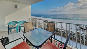Un balcón con vista a la playa, una mesa, sillas y una barandilla.