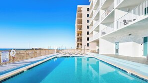 Una piscina azul cristalina con un muelle de madera y un cartel que indica las normas de la piscina.