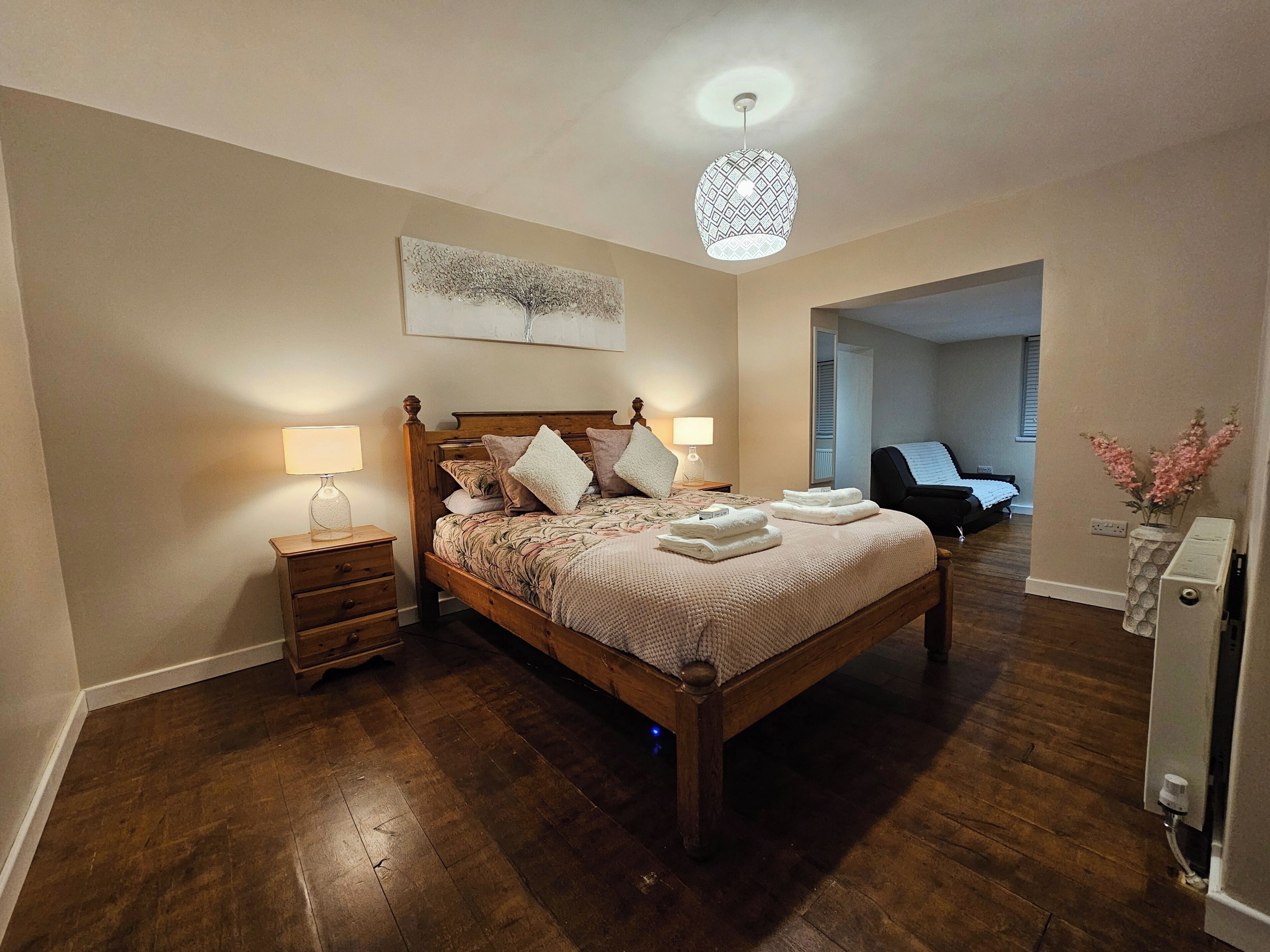 A bedroom with a wooden bed, bedside lamps, a ceiling light fixture, and a painting on the wall.