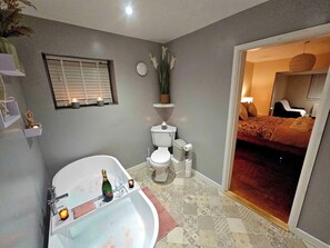 A bathroom with a bathtub, toilet, and shower. There is a bed visible through an open door in the adjacent room. - Seaside Bliss Retreat - 5 Bedroom House (Holyhead)