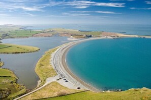 A coastal landscape with a large body of water, a curved shoreline, and green fields. - Seaside Bliss Retreat - 5 Bedroom House (Holyhead)