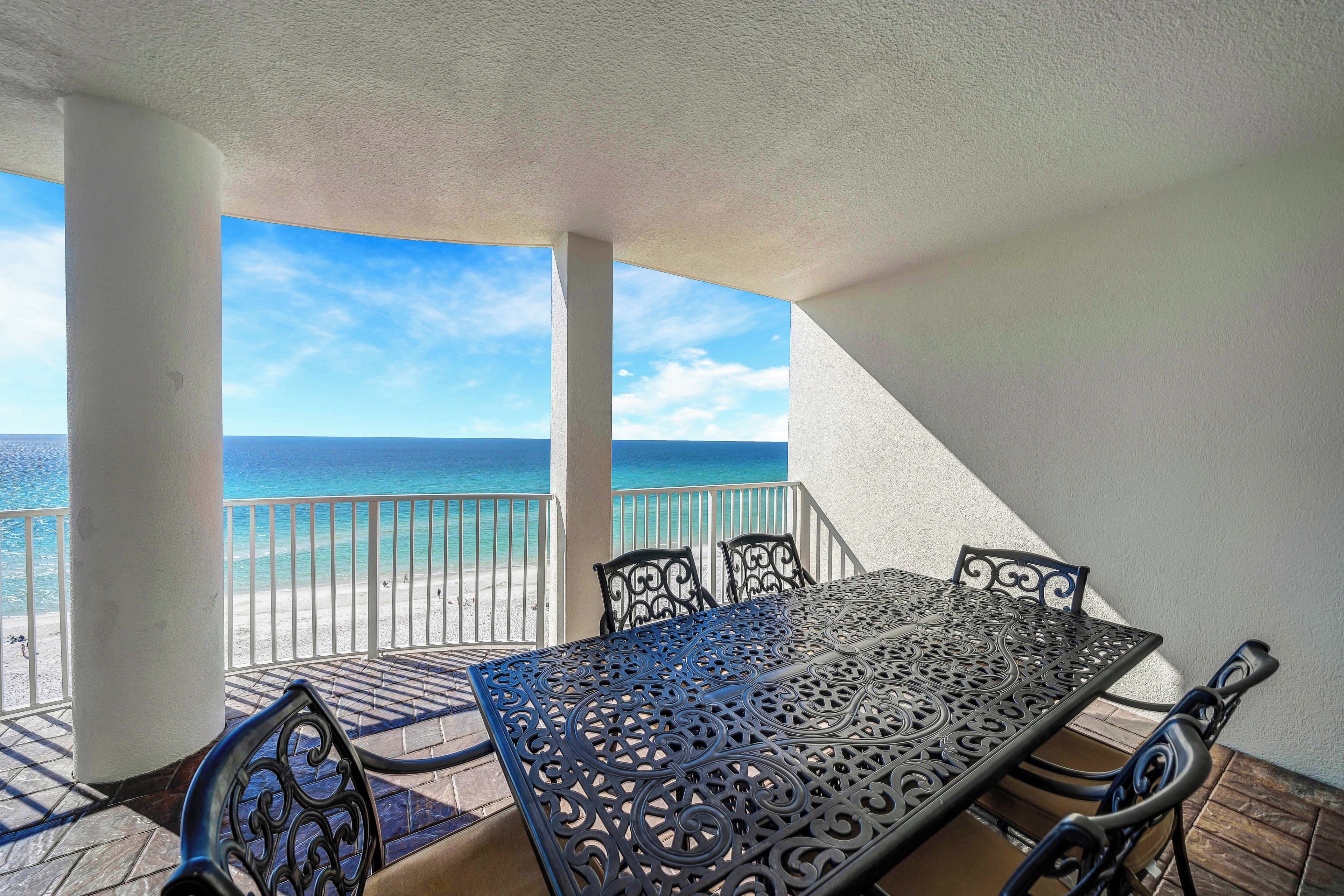 A balcony with a table and chairs overlooking a beach.