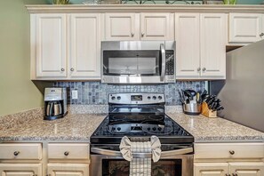 A kitchen with a stainless steel microwave, a coffee maker, and a stove. - Ocean Ritz 902 Beachfront, Heated Pool, Hot Tub, Gym, FREE Daily Golf&Perks! (Panama City Beach)
