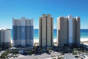 A beachfront hotel with multiple high-rise buildings, a parking area, and a clear view of the ocean. - Ocean Ritz 902 Beachfront, Heated Pool, Hot Tub, Gym, FREE Daily Golf&Perks! (Panama City Beach)