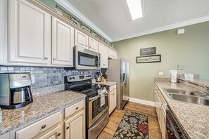 A kitchen with white cabinets, a microwave, stove, refrigerator, and a coffee maker. - Ocean Ritz 902 Beachfront, Heated Pool, Hot Tub, Gym, FREE Daily Golf&Perks! (Panama City Beach)