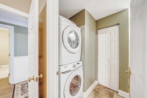 A laundry room with a stacked washer and dryer, a door, and a patterned rug.