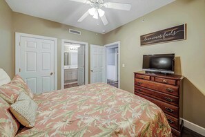 A bedroom with a bed, a dresser, a television, and a ceiling fan.