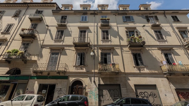 A multi-story building with balconies, windows, and a garage door with graffiti. - Filiberto Studio by Wonderful Italy (Turin)