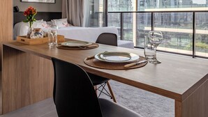 A modern hotel room with a large bed, a dining area with a wooden table, and a view of the cityscape through large windows. - PERFECT STUDIO ITAIM / FARIA LIMA PARKING SPACE  (Vila Olímpia São Paulo)