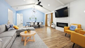 A modern living room with a sofa, coffee table, and yellow armchairs. There is a dining area with a table and chairs, a fireplace, and a TV mounted on the wall. - Best of Desoto 4BR,3BA with Pool, HotTub, Cinema (DeSoto)