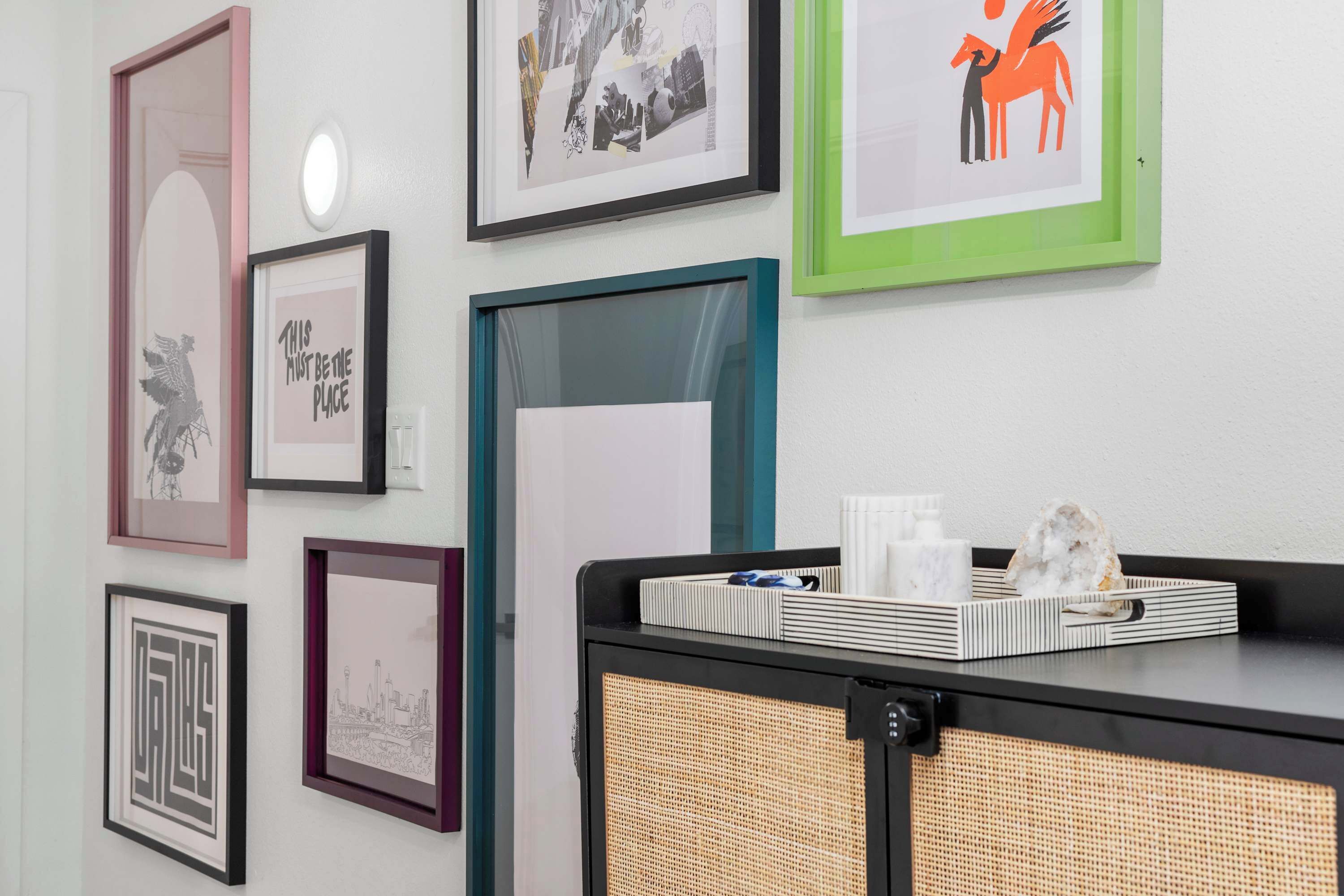A wall with various framed artworks, a wicker basket, and a tray with items on a black surface.