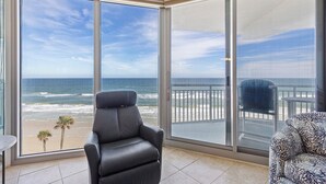 A balcony with a view of the ocean, a black chair, and a patterned sofa.