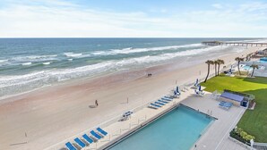 A beach view with a pool and lounge chairs.