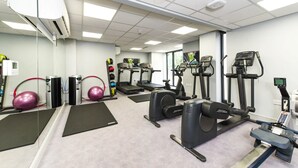 Une salle de sport équipée de tapis de course, de vélos elliptiques et de ballons d’exercice.