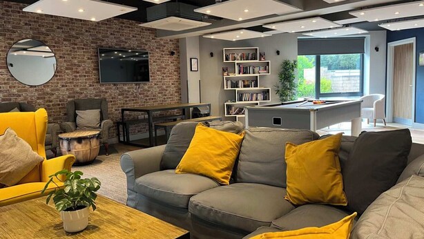 Un salon moderne avec un mur en briques, un téléviseur à écran plat, une table de billard et une bibliothèque.