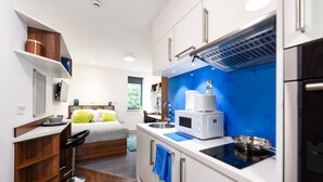 Une chambre d’hôtel de taille réduite, comprenant un lit, une kitchenette, une petite salle de bain et une fenêtre.