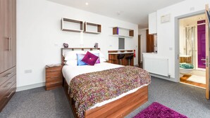 A modern bedroom with a wooden bed, a desk, and a bathroom visible through an open door. - Chapel Heights in Durham (Durham)