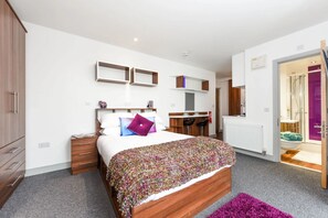 Une chambre à coucher moderne avec un lit en bois, un bureau et une salle de bain visible à travers une porte ouverte.