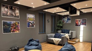 Un espace de détente moderne avec un canapé gris, deux fauteuils en forme de poire bleus, une table basse en bois et des affiches accrochées aux murs.