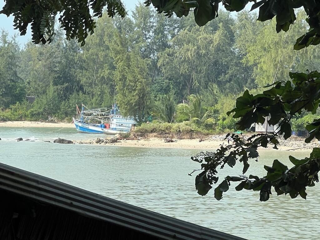 A boat docked near a beach with dense trees in the background.