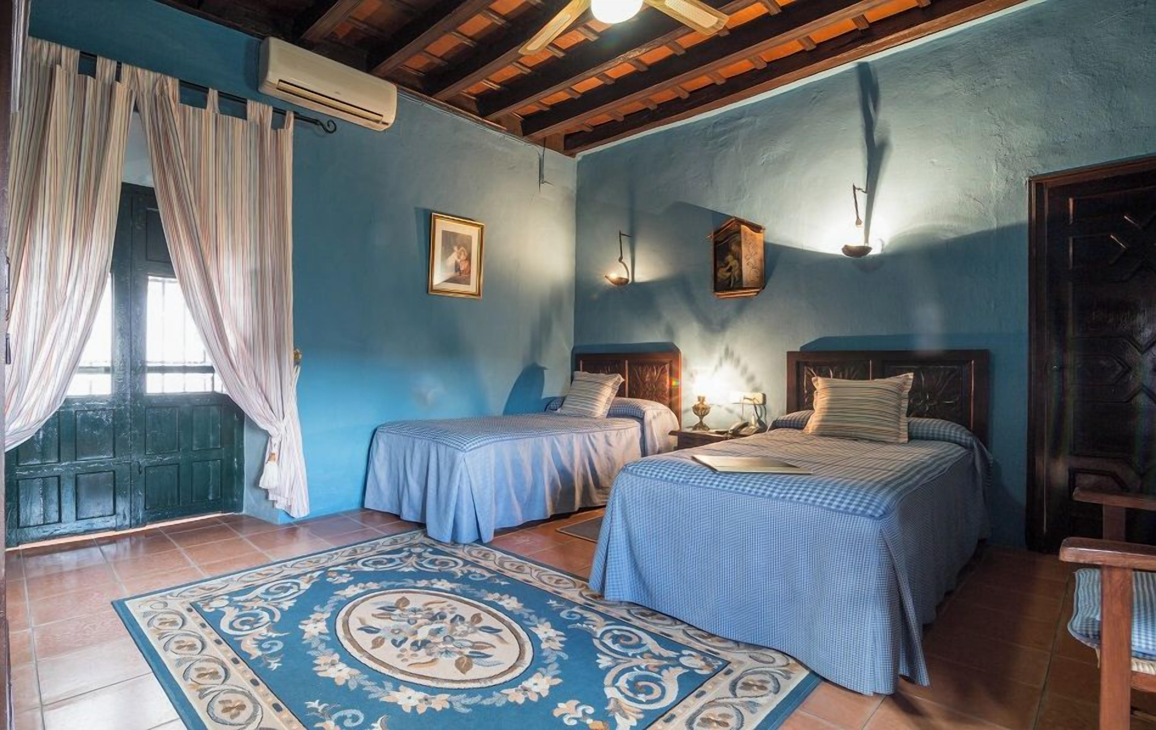 A room with two beds, a patterned rug, and a window with curtains.