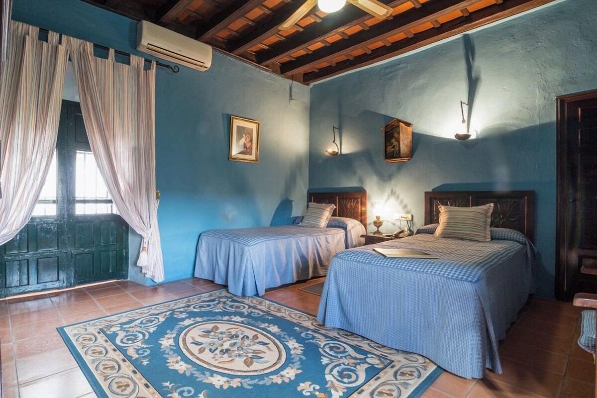 A room with two beds, a patterned rug, and a window with curtains.